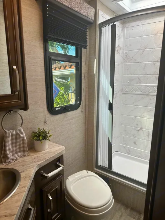 Compact and functional RV rental bathroom featuring a vanity, toilet, and a clean shower stall with marble-patterned walls and a window.. Jayco Melbourne 2022