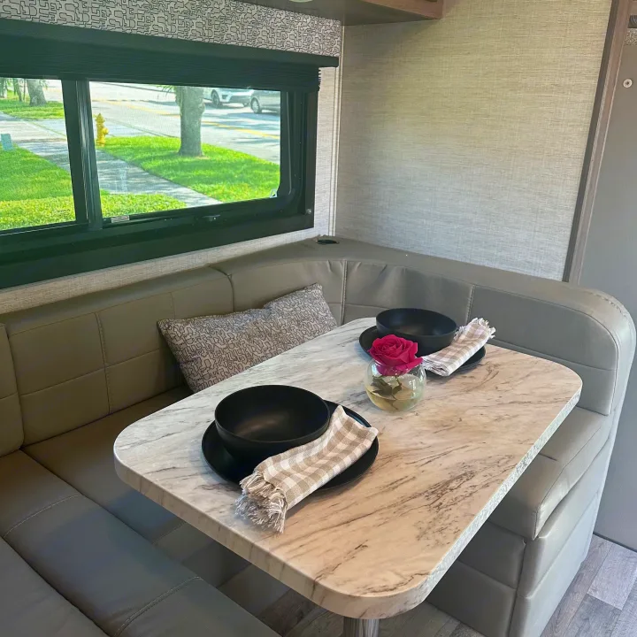 Experience comfort in this RV rental's dining area. Features a cozy booth, marble table, place settings, and a scenic window.. Jayco Melbourne 2022