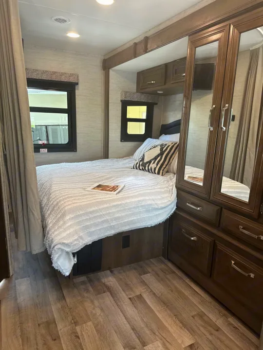 Cozy RV rental bedroom featuring a queen bed with white bedding, wood-look flooring, and mirrored storage.. Jayco Melbourne 2022