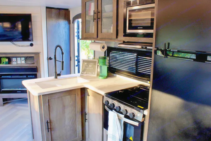 This RV rental kitchen features a sink, stove, microwave, fridge, and stylish decor, perfect for your next adventure.. Forest River Wildwood 2021