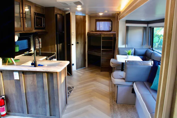 Spacious RV rental interior featuring a modern kitchen island, U-shaped dining area, and bunk beds in light wood tones.. Forest River Wildwood 2021