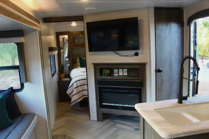 Inside a stylish RV rental, featuring a cozy living area, bedroom, and kitchen with a sink and electric fireplace.. Forest River Wildwood 2021