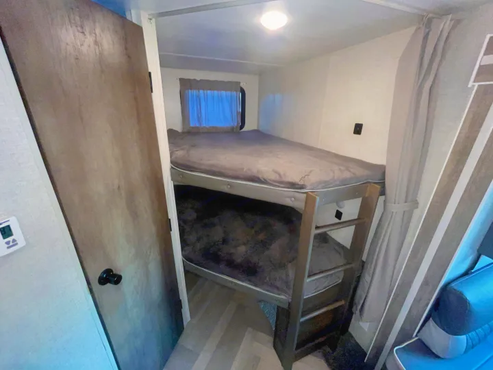 RV rental's compact sleeping area: stacked bunk beds with grey bedding, window, and door.. Forest River Wildwood 2021
