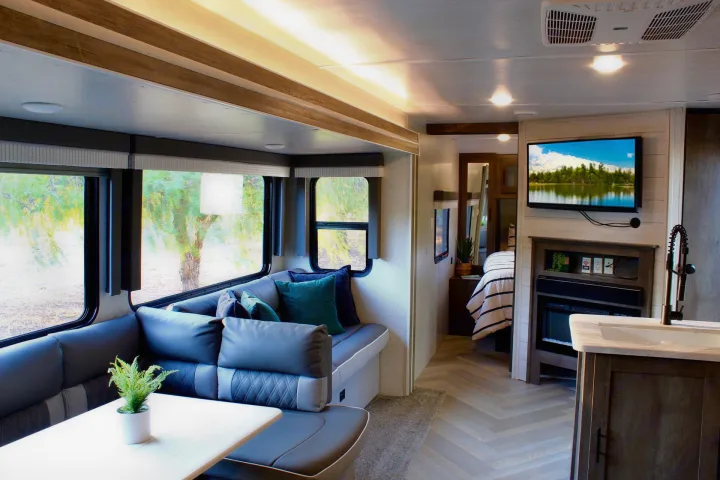 This modern RV rental features a bright living area with a large U-shaped sofa, TV, kitchen, and a cozy bedroom visible beyond.. Forest River Wildwood 2021