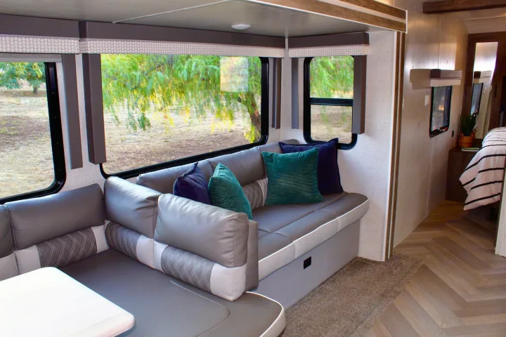 Modern RV rental interior: L-shaped dinette with large scenic windows, comfy pillows, and a glimpse of the bedroom. Perfect for travel.. Forest River Wildwood 2021