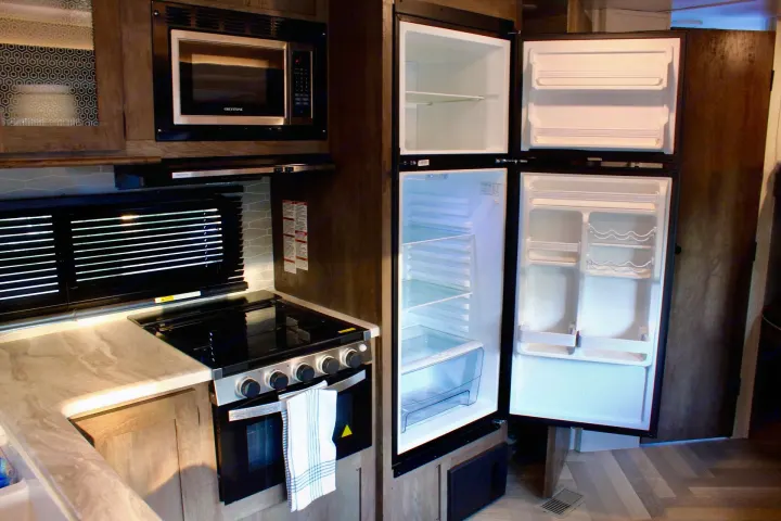 RV rental interior: A bright, modern kitchen with open refrigerator, microwave, gas stove/oven, and light counters.. Forest River Wildwood 2021