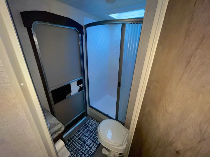 Inside an RV rental bathroom with toilet, shower, and small counter, featuring bright blue shower lighting.. Forest River Wildwood 2021