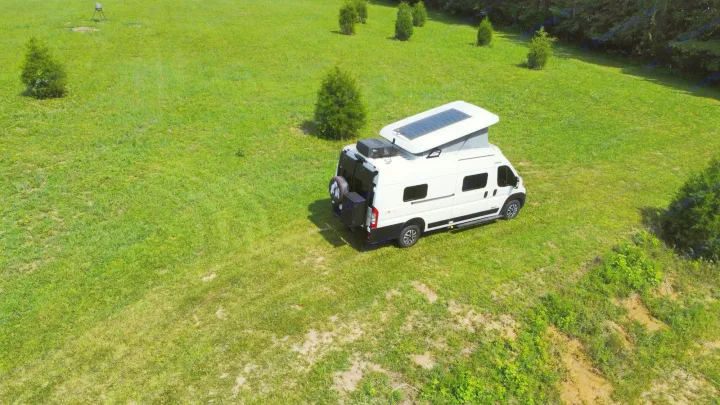 Experience freedom with an RV rental! This white Winnebago Solis camper van with solar panels is parked in a grassy field.. Winnebago Solis 2023