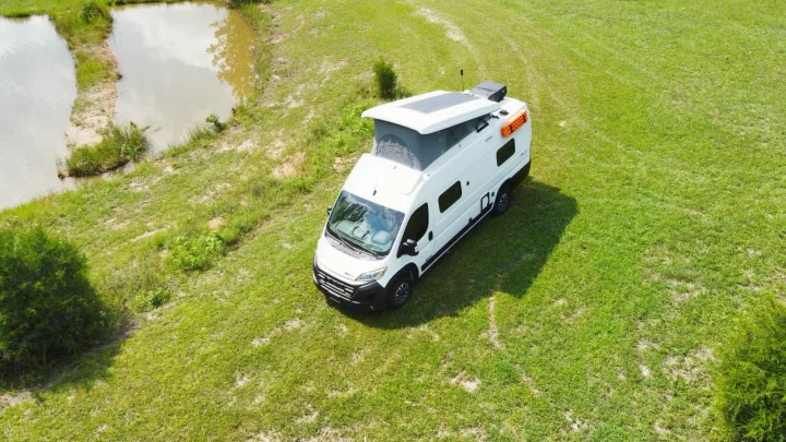 Aerial view of a white pop-top camper van in a grassy field next to a pond, ideal for RV rental adventures.. Winnebago Solis 2023