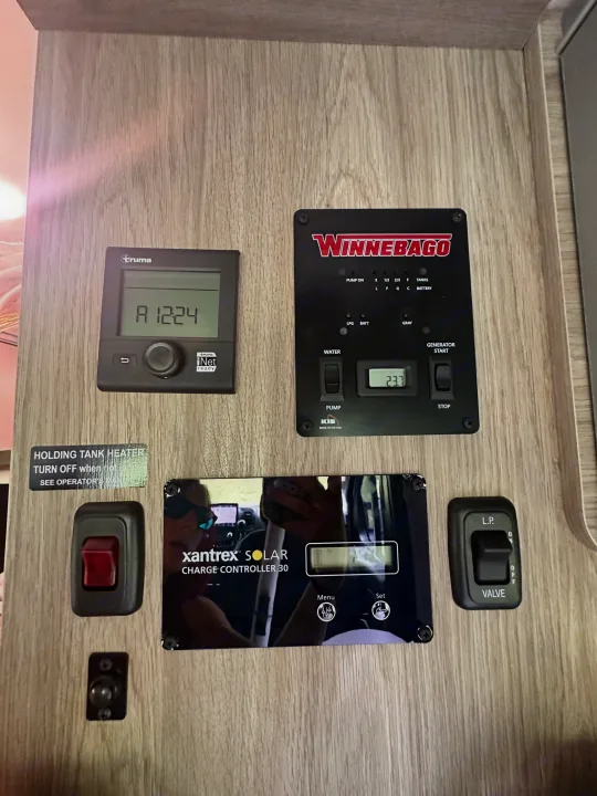 An RV rental control panel featuring various displays and switches for tank levels, solar charge, water pump, heater, and generator.. Winnebago Solis 2023