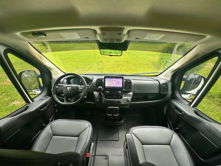 Detailed view of a modern **RV rental**'s front cabin, showing the dashboard, touchscreen, steering wheel, and seats.. Winnebago Solis 2023