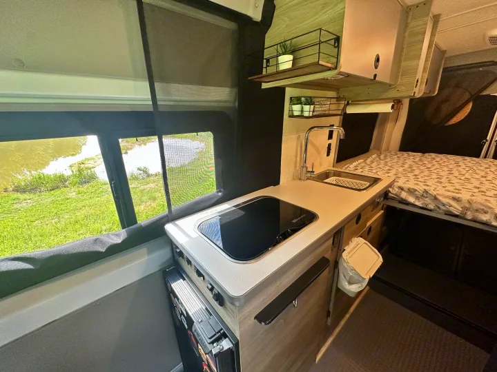 Experience an RV rental: compact interior with kitchenette (stove & sink), bed, and scenic window views. Ideal for travel.. Winnebago Solis 2023