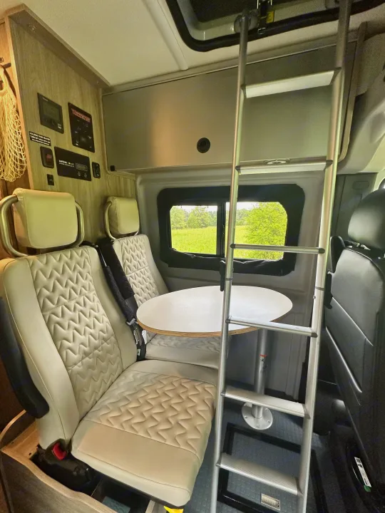 Inside a Winnebago RV rental: a compact interior with quilted seats, a dining table, and an access ladder.. Winnebago Solis 2023