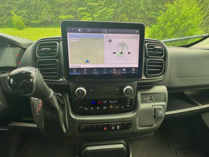 Dashboard of an RV rental: infotainment screen displays navigation, media, and 90°F outdoor temp. Includes climate controls and shifter.. Winnebago Solis 2023