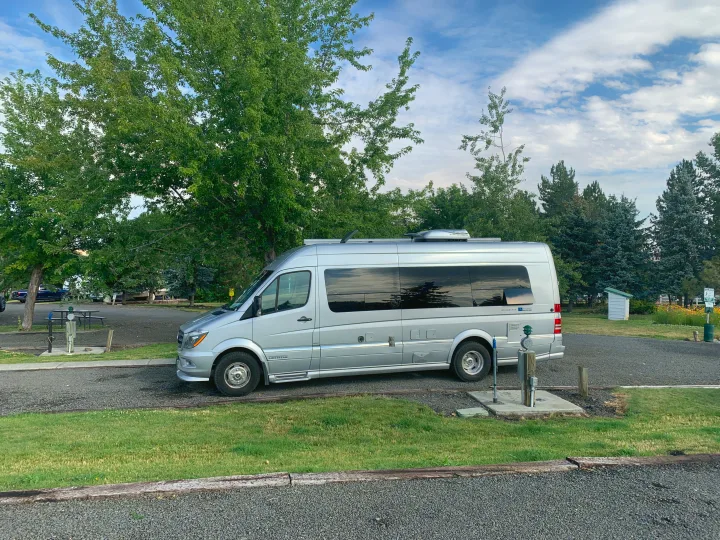 A silver Airstream Interstate RV rental parked on gravel at a leafy campsite with utility hookups. Perfect for travel!. Airstream Interstate 2017