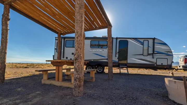 Sunny desert campsite features an rv rental, wooden pergola over a picnic table, and distant mountains under a blue sky.. Forest River Cherokee Alpha Wolf 2021