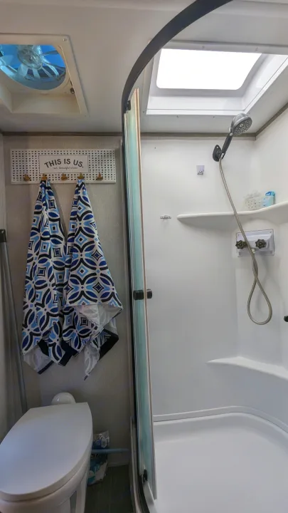 RV rental bathroom features shower, toilet, ceiling fan, and skylight. Blue patterned towels hang on a decorative rack.. Forest River Cherokee Alpha Wolf 2021