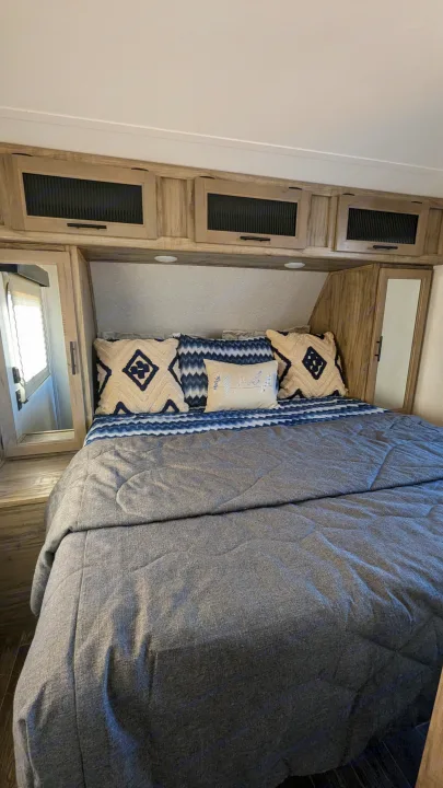 Cozy RV rental bedroom features a comfortable bed with decorative pillows, overhead storage, and mirrored cabinets, ideal for travel.. Forest River Cherokee Alpha Wolf 2021
