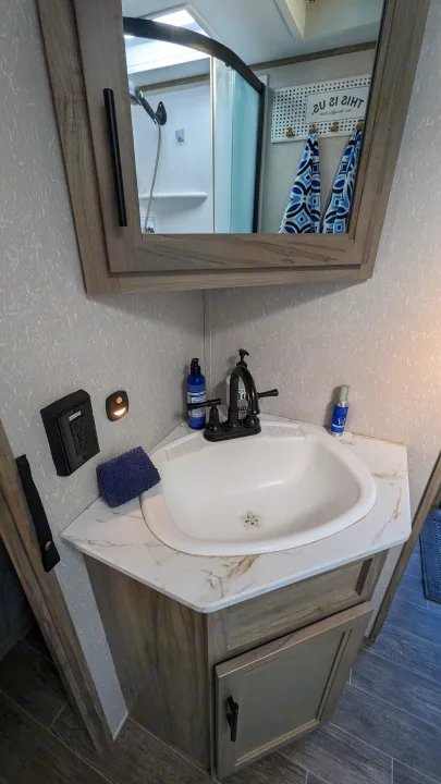 Compact RV rental bathroom features a corner sink, marble vanity, and mirror reflecting the shower.. Forest River Cherokee Alpha Wolf 2021