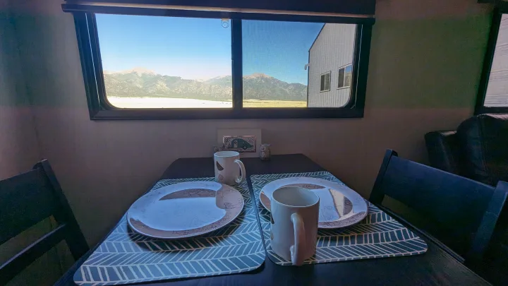 An RV rental dining area with a table set for two, offering a scenic mountain view. Ideal for travel.. Forest River Cherokee Alpha Wolf 2021