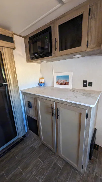 Modern RV rental kitchen with a microwave, spacious marbled counter, light wood cabinets, and wood-look flooring.. Forest River Cherokee Alpha Wolf 2021