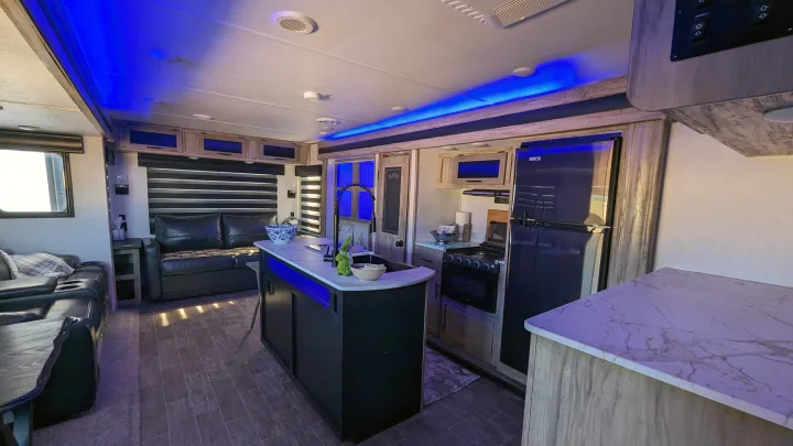 Spacious RV rental interior with modern kitchen, comfortable seating, and vibrant blue lighting.. Forest River Cherokee Alpha Wolf 2021
