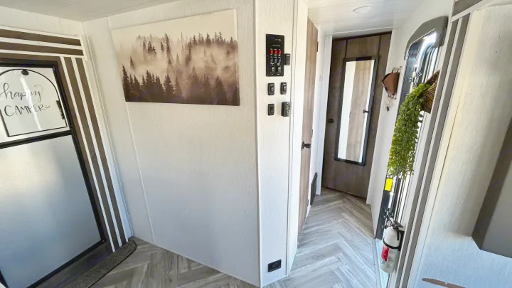 Bright RV rental interior featuring a large forest art print, control panel, and 'happy camper' refrigerator.. Forest River Wildwood 2022