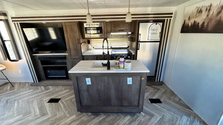 Modern RV rental interior featuring a kitchen island with sink, full kitchen appliances, TV, and electric fireplace.. Forest River Wildwood 2022