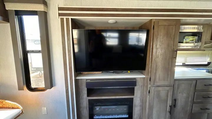 Spacious RV rental interior with entertainment setup (TV, fireplace) and well-equipped kitchen (microwave). Bright window.. Forest River Wildwood 2022