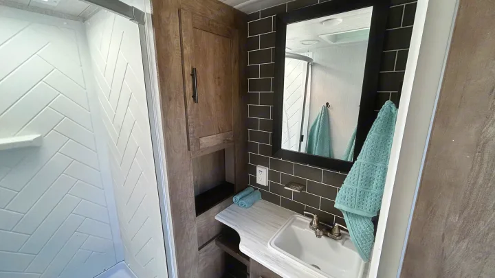 Modern RV rental bathroom showcasing a white herringbone shower, black subway tile backsplash, and a clean vanity with sink.. Forest River Wildwood 2022