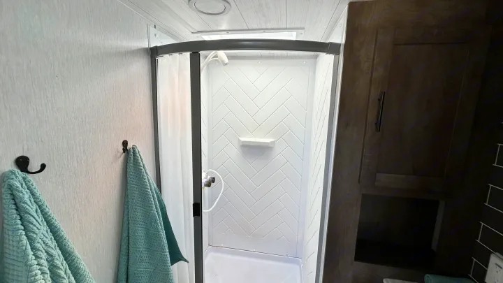 Compact RV rental bathroom with a white herringbone shower, light blue towels, and dark wood accents.. Forest River Wildwood 2022