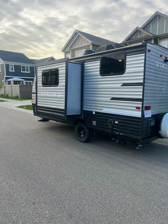Silver Viking travel trailer, an RV rental, parked on a residential street with houses in the background.. Viking 1706 2021