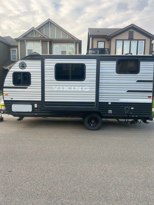 Black & silver Viking travel trailer, perfect for an RV rental or camping trip, parked on asphalt near homes.. Viking 1706 2021