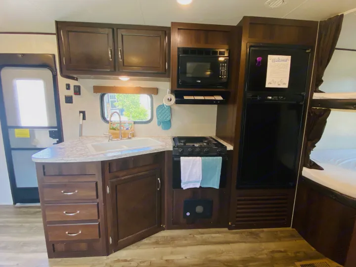 Experience a functional RV rental kitchen: sink, stove, microwave, fridge, and cozy bunk beds. A compact space for travel.. Jayco Jay Flight SLX 2018