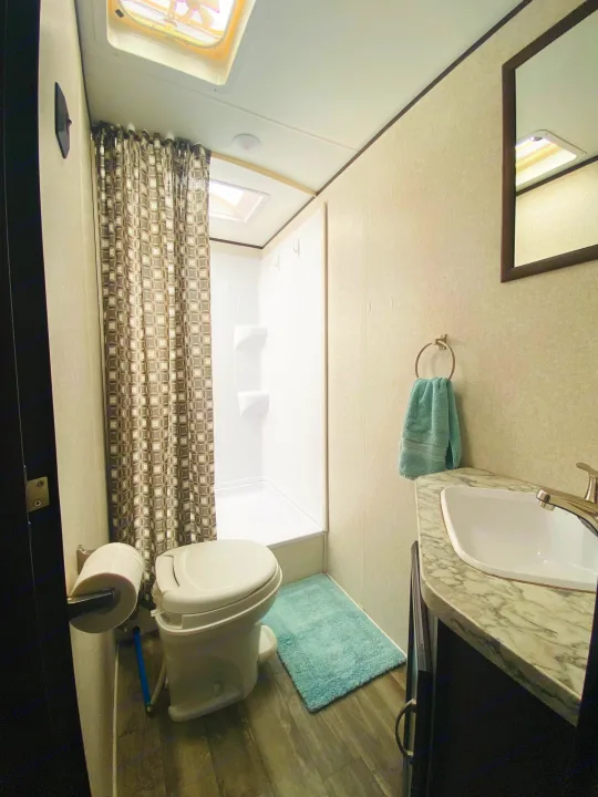 Compact RV rental bathroom features a shower, toilet, sink, mirror, and teal accents.. Jayco Jay Flight SLX 2018