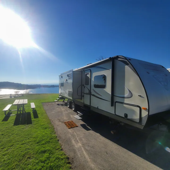 Scenic RV rental campsite by the lake with a picnic table on green grass. Perfect for a sunny getaway!. Winnebago Ultralite 2014