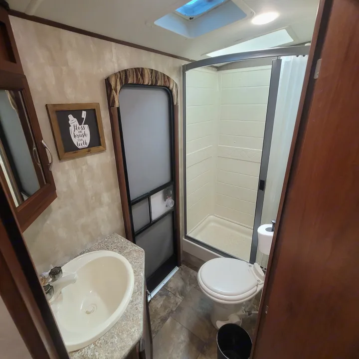 RV rental bathroom with warm wood accents, a functional sink, toilet, and standing shower. Ready for your trip!. Winnebago Ultralite 2014