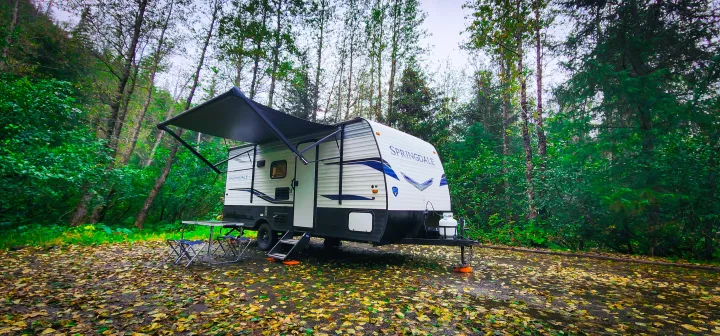 Fall camping RV rental: Springdale travel trailer parked under an awning in a lush, leaf-covered forest setting.. Keystone RV Springdale 2022