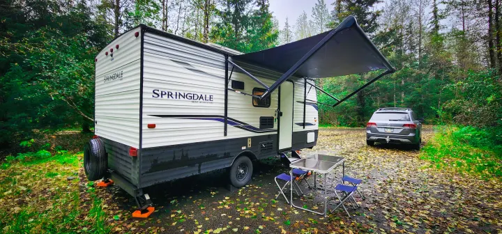 Enjoying nature with an RV rental: A Springdale Mini travel trailer is set up with an awning, table, and SUV at a wooded campsite.. Keystone RV Springdale 2022