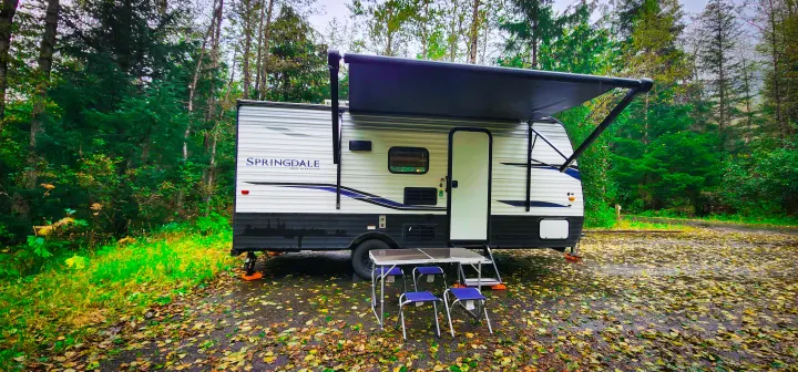 This RV rental is set up in a beautiful forest campground, complete with a cozy outdoor dining area under its awning.. Keystone RV Springdale 2022