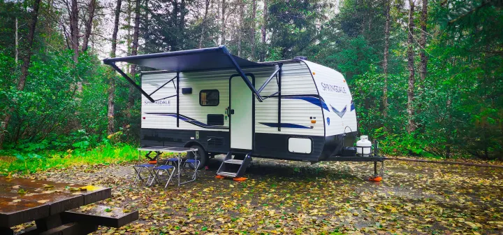 Enjoy nature with this rv rental! A Springdale travel trailer with awning extended is parked at a leafy, wet campsite in a forest.. Keystone RV Springdale 2022