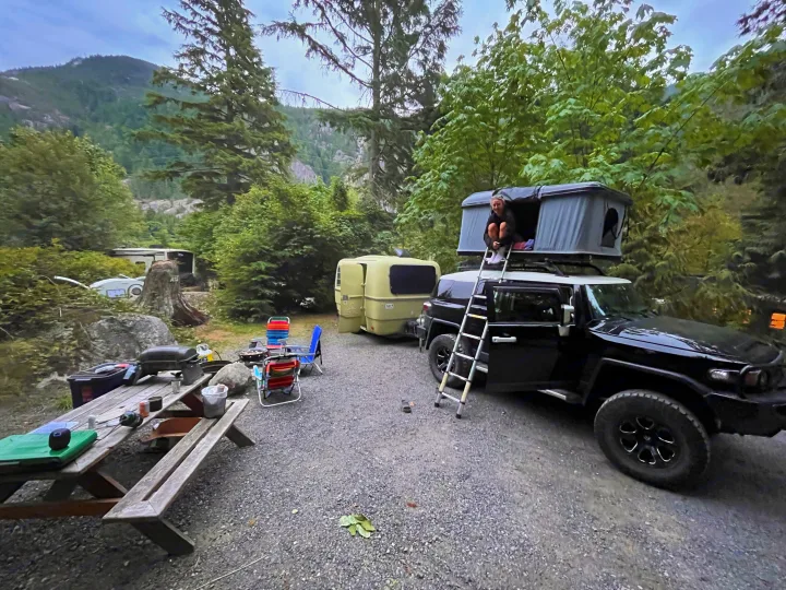 Mountain camping scene: An RV rental travel trailer, SUV with rooftop tent, and picnic area. Ready for outdoor adventure.. Trillium Rv 1300 1976