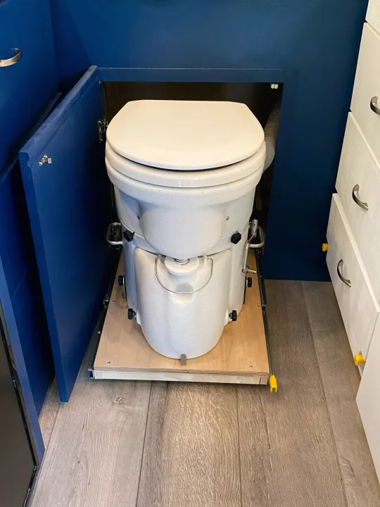 This RV rental features a pull-out composting toilet in a blue cabinet, optimizing space for comfortable mobile living.. Freightliner Sprinter 2020