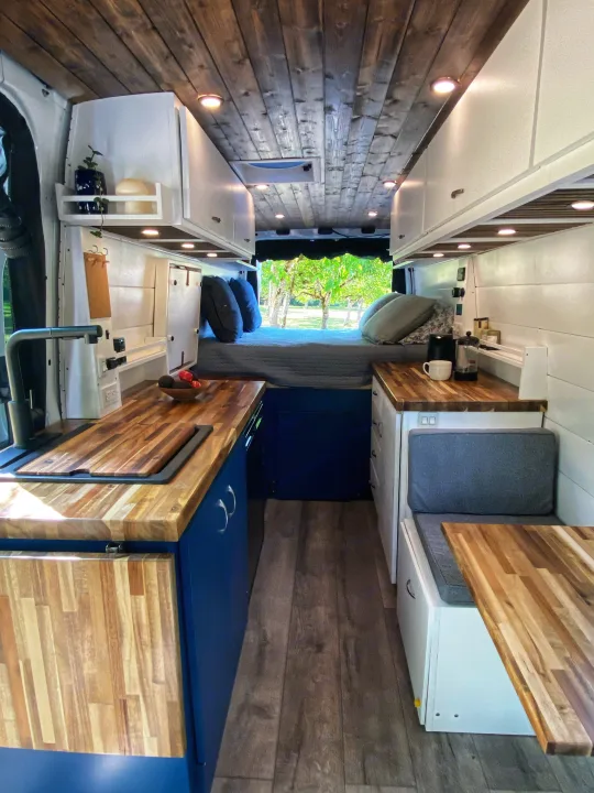 Bright RV rental interior: custom camper van with wood ceiling, full kitchen, cozy bed, and dining area.. Freightliner Sprinter 2020