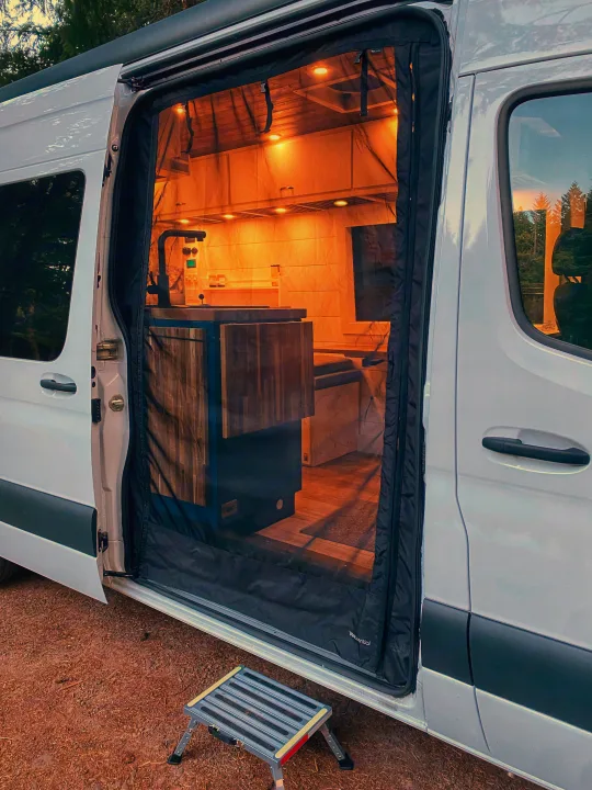 Cozy **RV rental** interior: a well-lit camper van kitchen and living space seen through an open side door with a screen.. Freightliner Sprinter 2020
