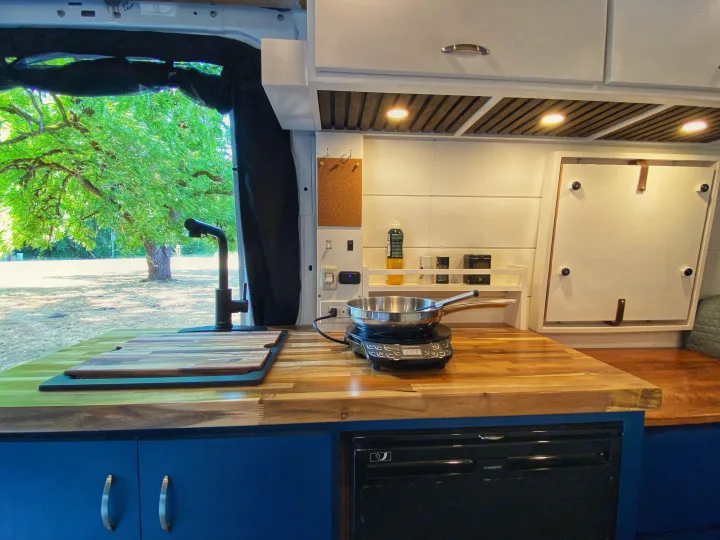 RV rental kitchen view: spacious butcher block counter, induction cooktop, sink, fridge, and green views outside.. Freightliner Sprinter 2020