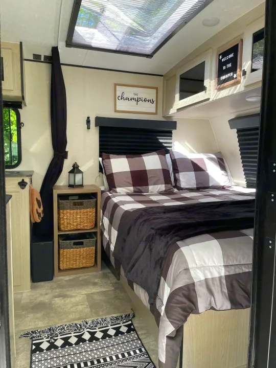 Cozy rv rental bedroom features a comfy plaid bed, woven baskets, and charming wall decor under a skylight.. Coachmen Apex Nano 2023