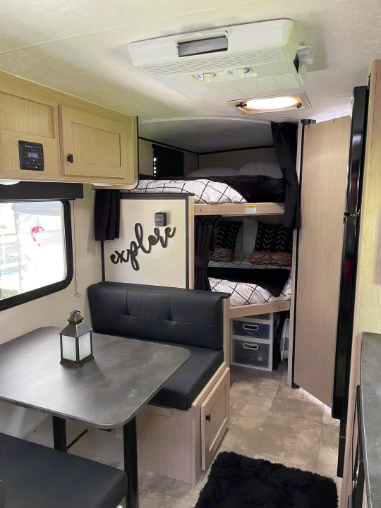 Cozy RV rental interior: modern dinette, black/white bunk beds with curtains, and a compact living area.. Coachmen Apex Nano 2023
