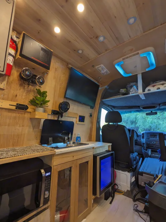 Cozy custom RV rental interior with a compact kitchen, living space, microwave, and mini-fridge for comfortable travel.. Mercedes Benz Sprinter 2500 2014