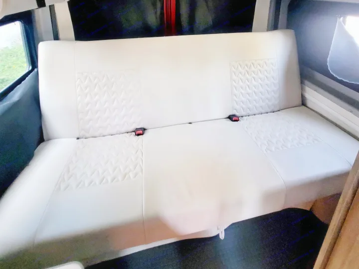 Off-white bench seat with zigzag patterns & seatbelts in an RV rental interior.. Winnebago Solis 2022